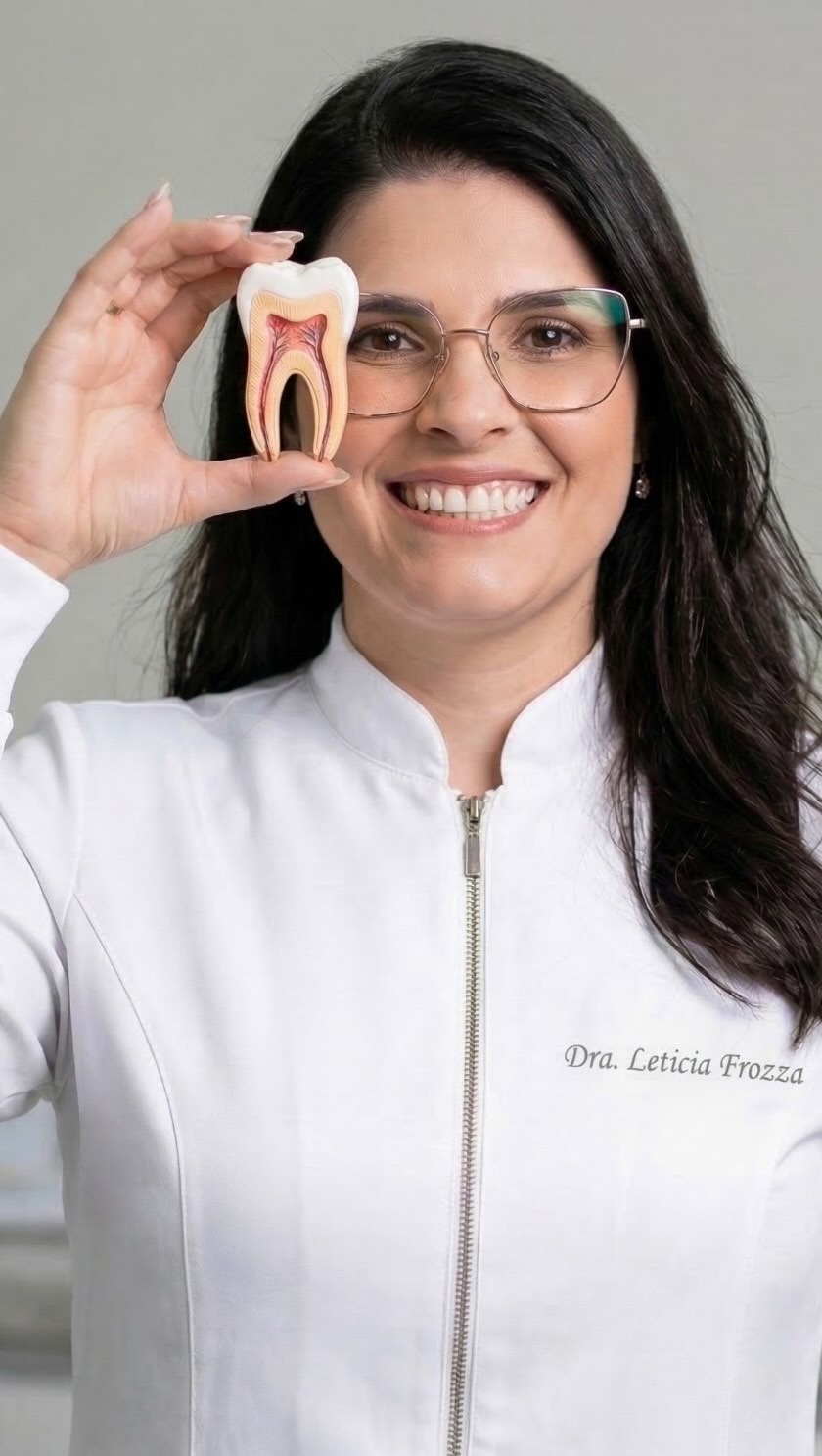 Dra. Leticia Frozza segurando um modelo de dente e sorrindo
